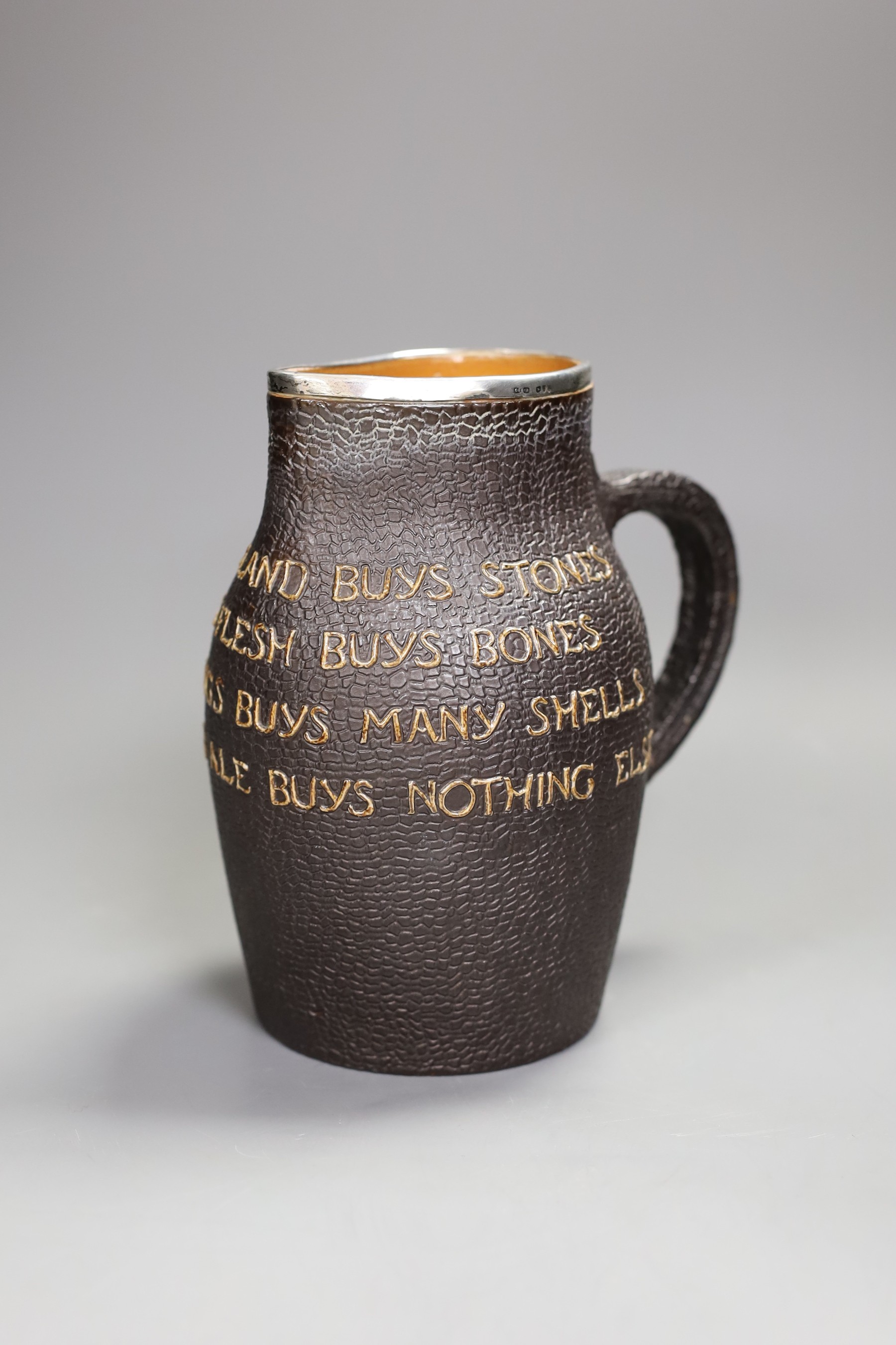 A Doulton Lambert leather-effect jug, ‘He Who Buys Good Ale Buys Nothing Else’, with silver mount, 19cm tall